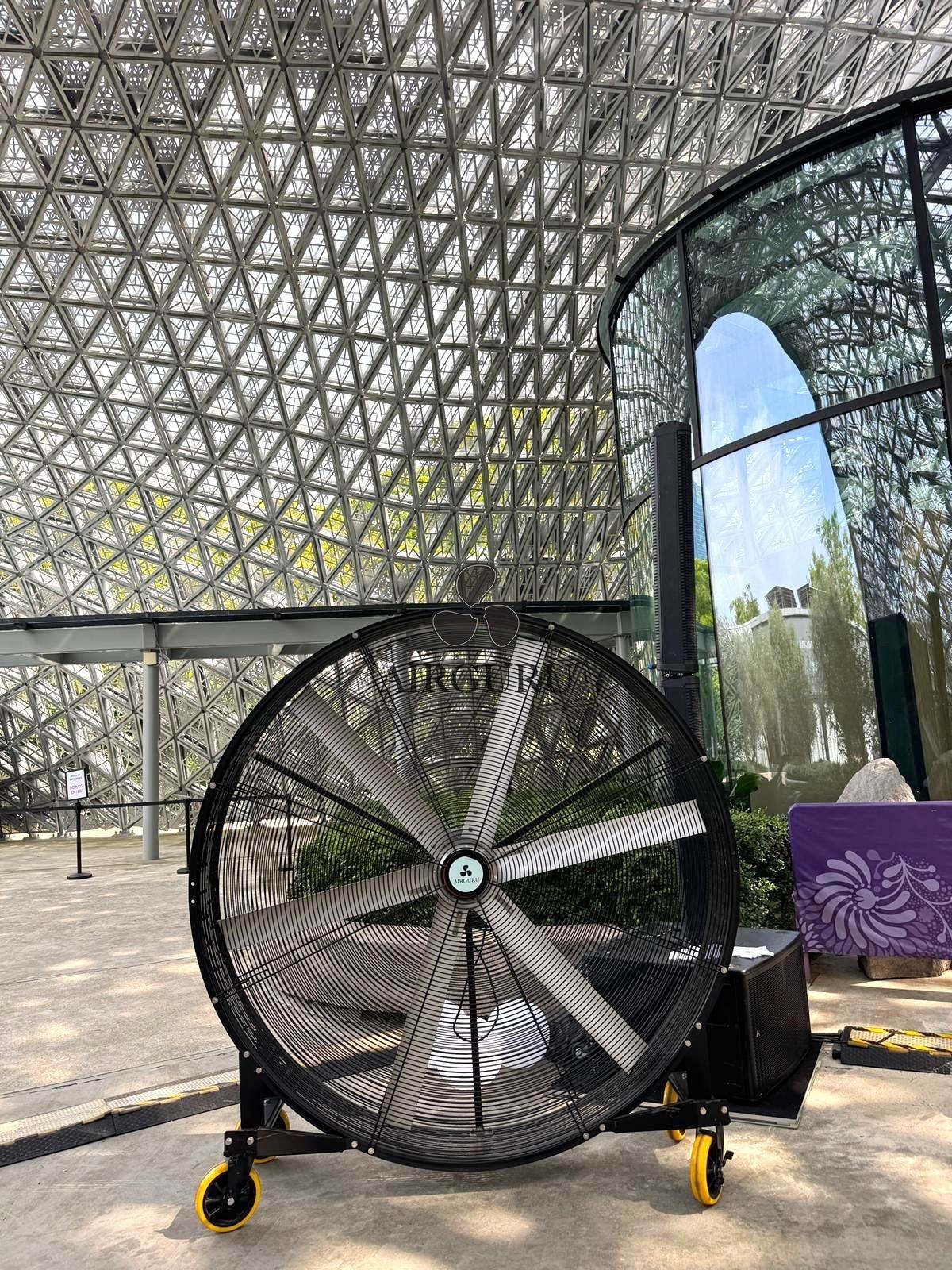 Airguru giant fan inside a glass pavilion beside a patterned wall