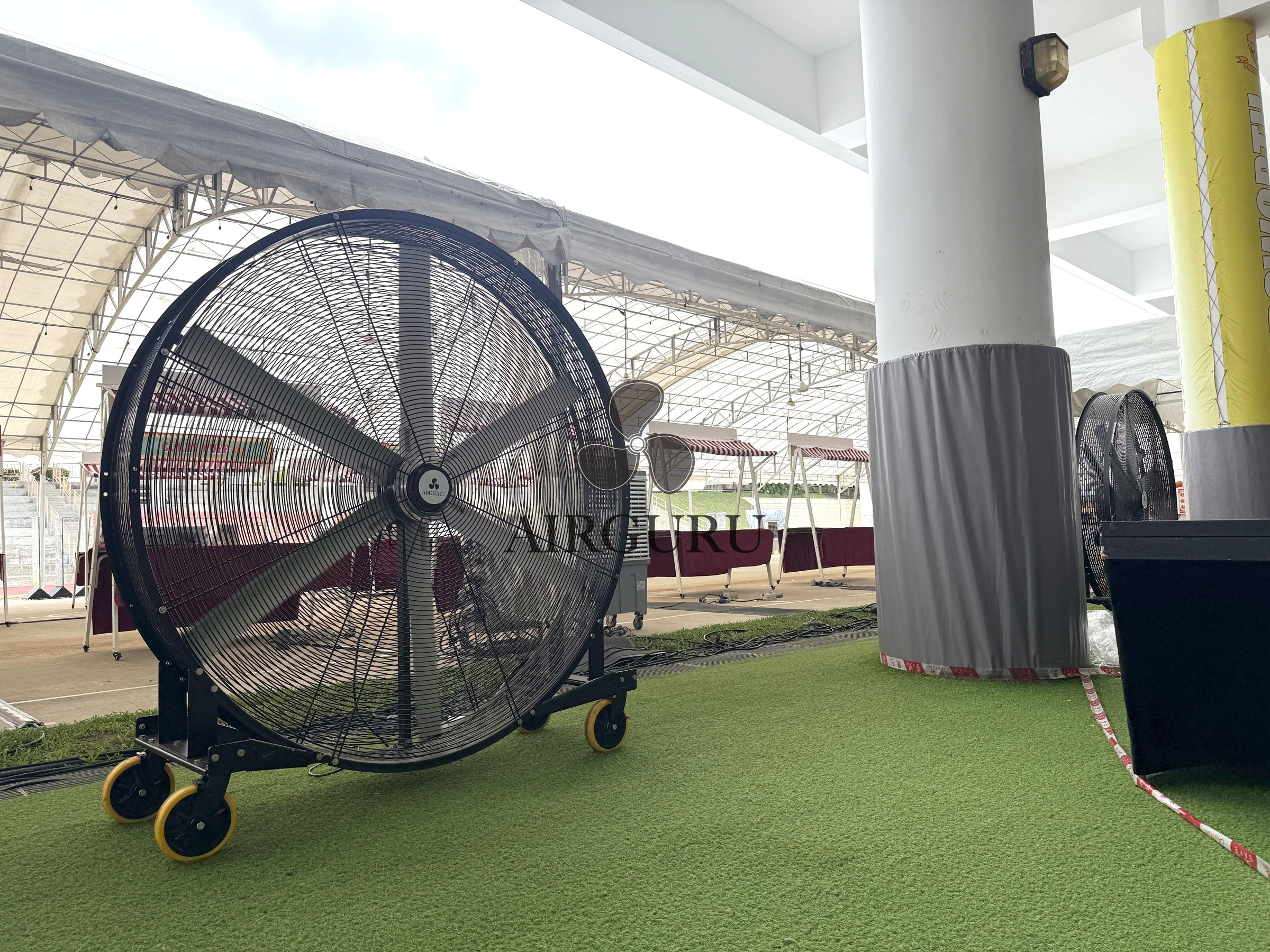 Airguru industrial fan on artificial turf beneath a sheltered event roof