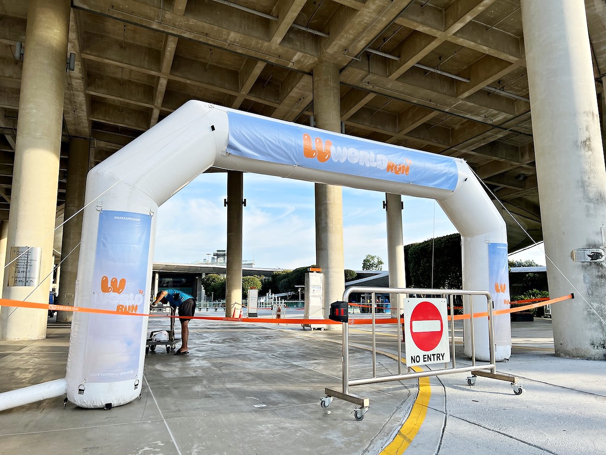 White event arch beneath a sheltered walkway with barriers marking the route